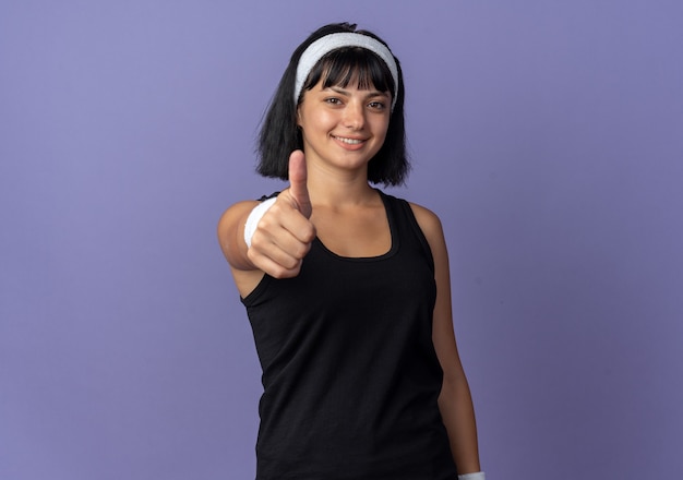 Chica joven fitness con diadema mirando a la cámara sonriendo seguros mostrando los pulgares para arriba