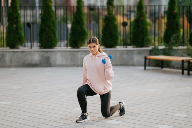 Chica joven fitness haciendo ejercicios con pesas en el parque de la ciudad