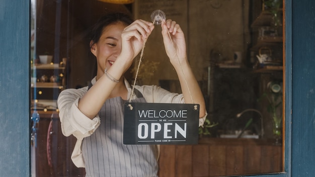 Chica joven gerente cambiando un cartel de cerrado a abierto en la cafetería de la puerta mirando afuera esperando clientes después del cierre.