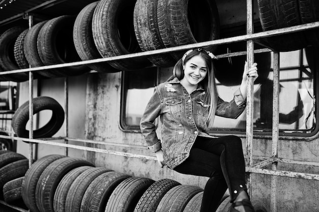 Chica joven hipster en chaqueta de jeans y pañuelo en la cabeza en la zona de montaje de neumáticos