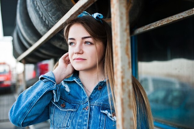 Chica joven hipster en chaqueta de jeans y pañuelo en la cabeza en la zona de montaje de neumáticos