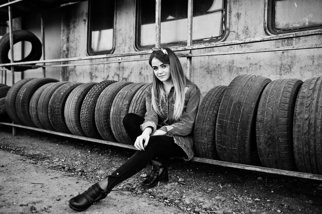 Chica joven hipster en chaqueta de jeans y pañuelo en la cabeza en la zona de montaje de neumáticos