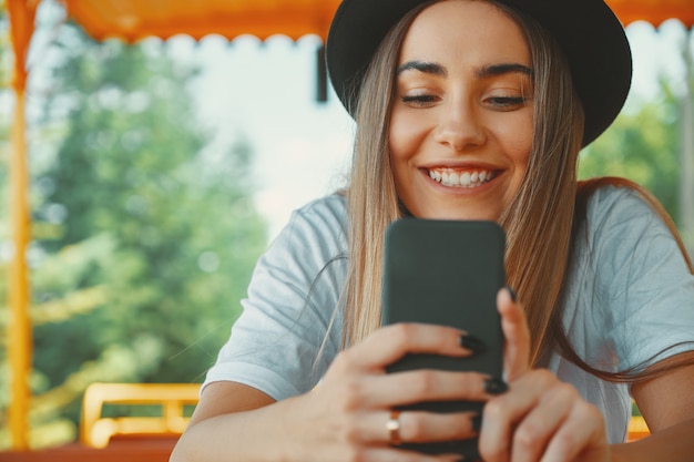 Chica joven inconformista en sombrero de moda con smartphone en manos