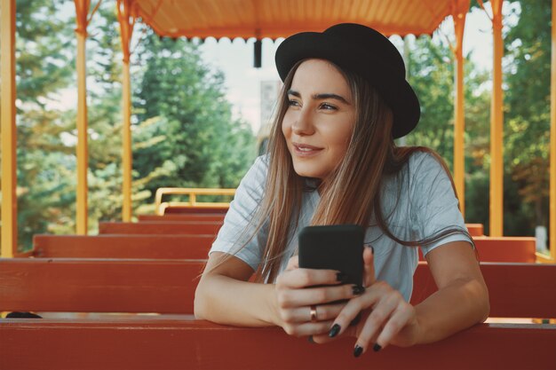 Chica joven inconformista en sombrero de moda con smartphone