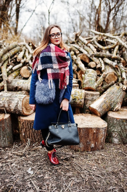 Chica joven inconformista usar abrigo y bufanda con bolso contra tocones de madera en madera