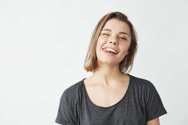 Chica joven linda divertida que sonríe guiñando un ojo mostrando la lengua.