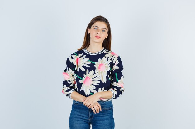 Chica joven con las manos delante de ella en un suéter floral, jeans y una linda vista frontal.
