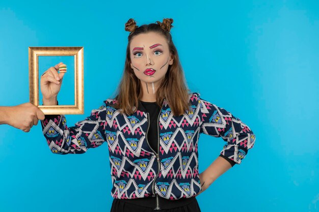 Chica joven con maquillaje de fantasía con caramelo de azúcar en marco vacío. foto de alta calidad