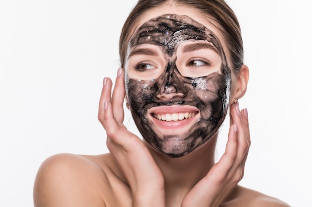 Chica joven con una máscara cosmética negra en su rostro con un cepillo aislado en una pared blanca