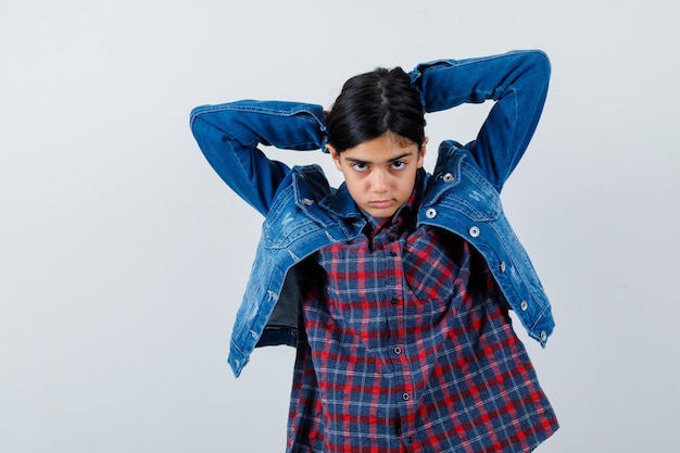 Chica joven metiendo el pelo en camisa a cuadros y chaqueta de mezclilla y luciendo bonita.