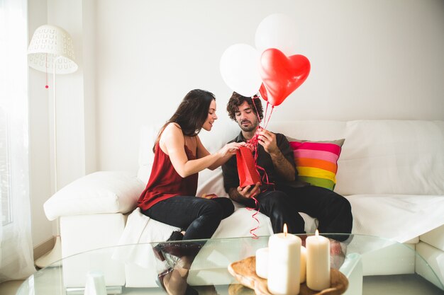 Chica joven mirando una bolsa roja mientras su novio sujeta globos rojos y blancos
