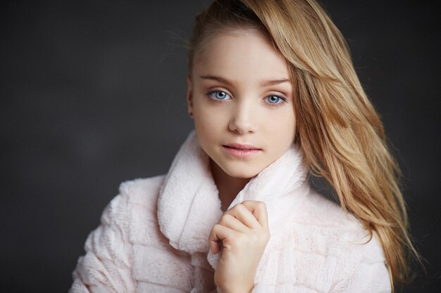 Chica joven de moda con ojos azules posando en bata blanca sobre fondo oscuro.