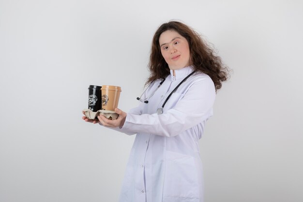 chica joven modelo en uniforme blanco sosteniendo un cartón con tazas de café.