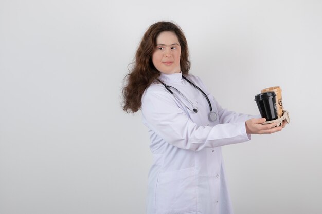 chica joven modelo en uniforme blanco sosteniendo un cartón con tazas de café.