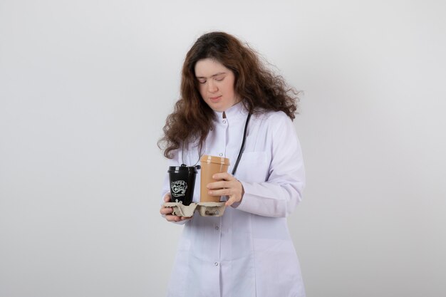 chica joven modelo en uniforme blanco sosteniendo un cartón con tazas de café.