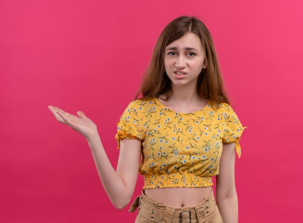 Chica joven molesta que muestra la mano vacía en el espacio rosa aislado
