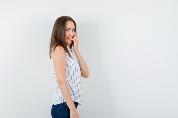 Chica joven mordiéndose las uñas en camiseta, jeans y mirando avergonzado.