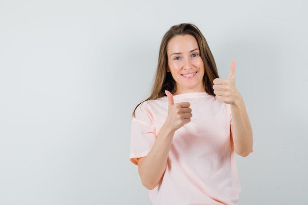 Chica joven mostrando doble pulgar hacia arriba en camiseta rosa y mirando alegre, vista frontal.