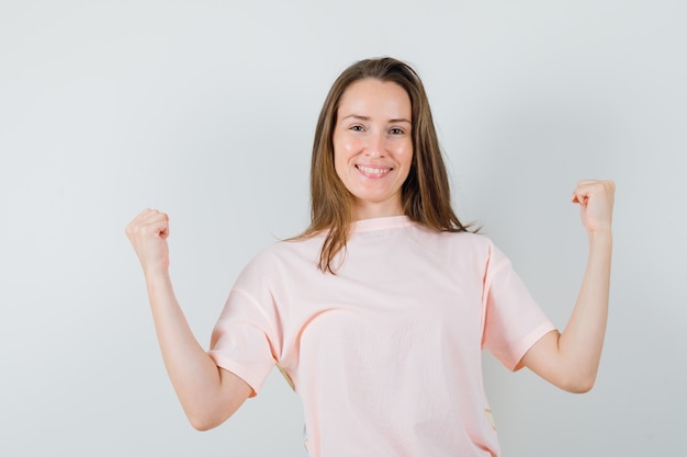 Chica joven mostrando gesto de ganador en camiseta rosa y mirando alegre