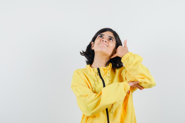 Chica joven mostrando gesto de llamarme en chaqueta de bombardero amarilla y mirando emocionado.