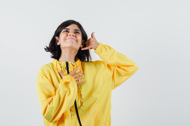 Chica joven mostrando gesto de llamarme en chaqueta de bombardero amarilla y mirando emocionado.