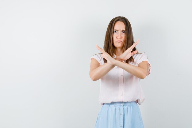 Chica joven mostrando gesto de parada en camiseta, falda y mirando nerviosa. vista frontal.
