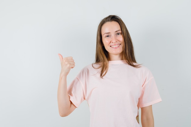 Chica joven mostrando el pulgar hacia arriba en camiseta rosa y mirando alegre
