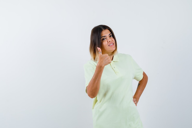 Foto gratuito chica joven mostrando el pulgar hacia arriba, sosteniendo la mano en la cintura en camiseta y luciendo confiada. vista frontal.