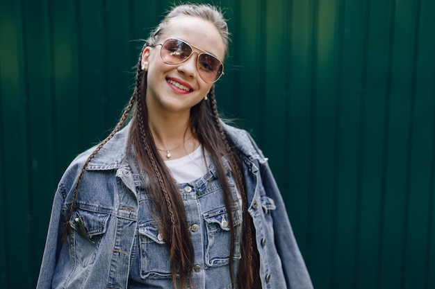 Chica joven muy atractiva en ropa de mezclilla en gafas sobre un fondo verde oscuro simple con lugar vacío para el texto