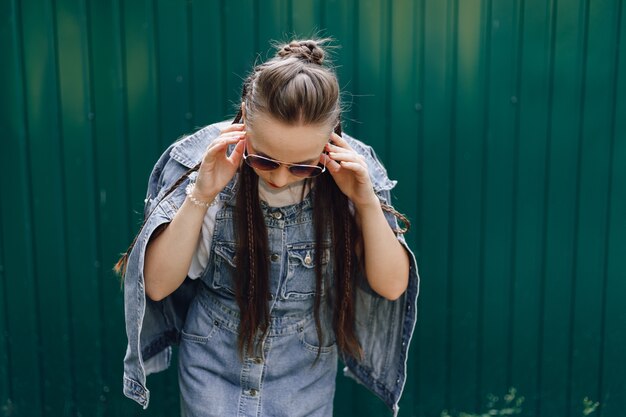 Chica joven muy atractiva en ropa de mezclilla en gafas sobre un fondo verde oscuro simple con lugar vacío para el texto