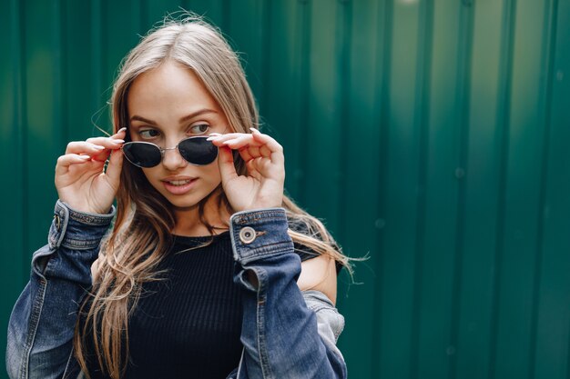 Chica joven muy atractiva en ropa de mezclilla en gafas sobre un fondo verde oscuro simple con lugar vacío para el texto