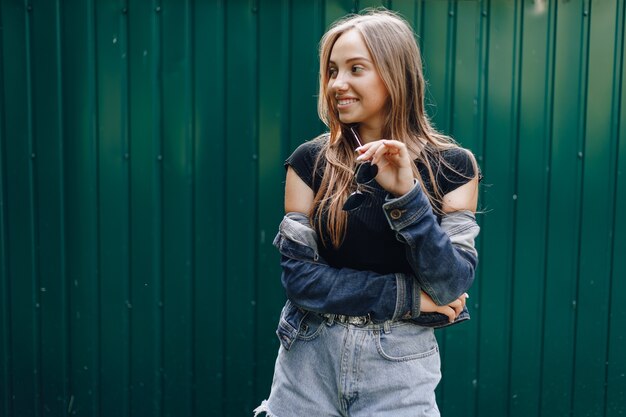 Chica joven muy atractiva en ropa de mezclilla en gafas sobre un fondo verde oscuro simple con lugar vacío para el texto