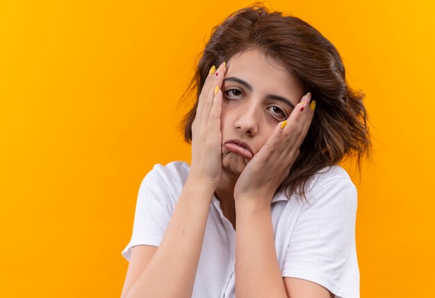 Chica joven con pelo corto vistiendo polo blanco con aspecto cansado y molesto tocando la cara con las manos