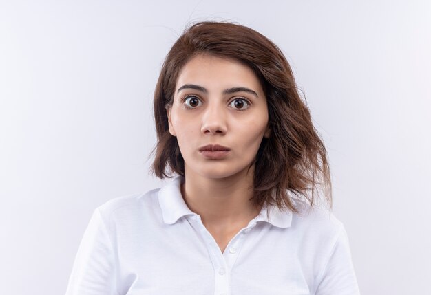 Chica joven con pelo corto vistiendo polo blanco mirando a cámara sorprendido y asombrado