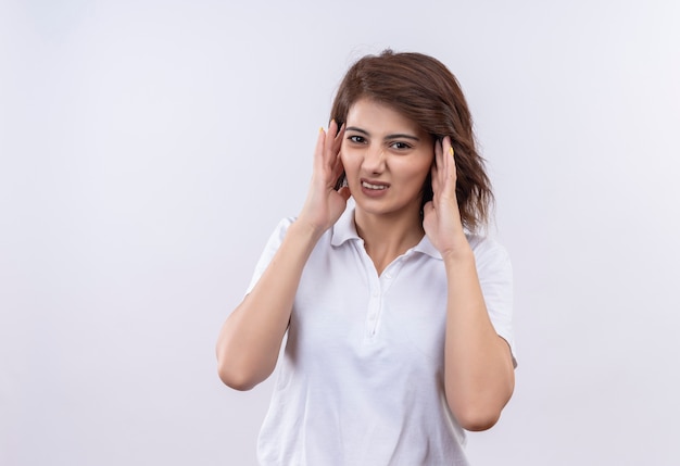 Chica joven con pelo corto vistiendo polo blanco mirando cansado rouching cabeza sufre de dolor de cabeza