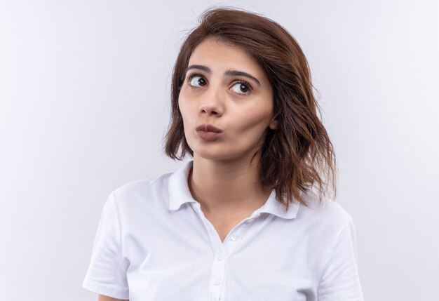 Foto gratuita chica joven con pelo corto vistiendo polo blanco mirando a un lado desconcertado