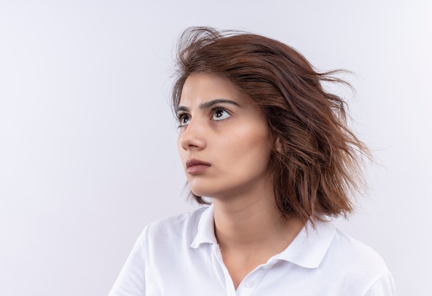 Foto gratuita chica joven con pelo corto vistiendo polo blanco mirando a un lado con expresión triste en la cara