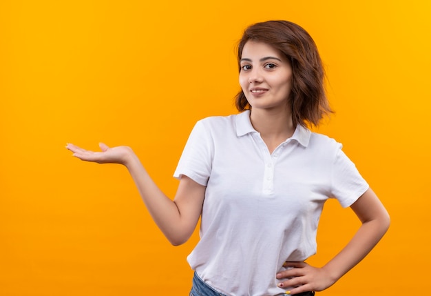 Chica joven con pelo corto vistiendo polo sonriendo confiado presentando con el brazo de la mano