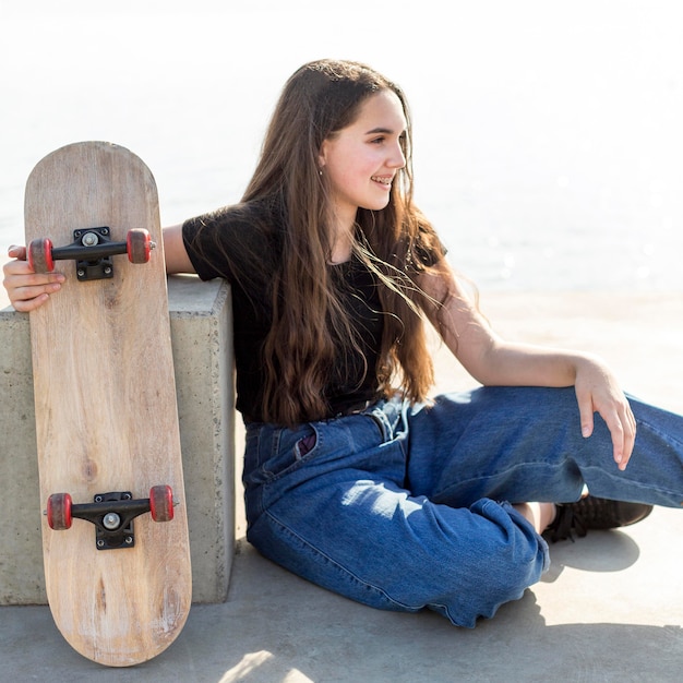 Foto gratuita chica joven con el pelo largo sosteniendo su patineta al aire libre