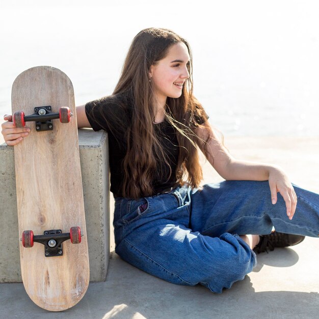 Chica joven con el pelo largo sosteniendo su patineta al aire libre