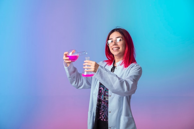 Chica joven con pelos rosados sosteniendo matraces químicos y haciendo reacción.