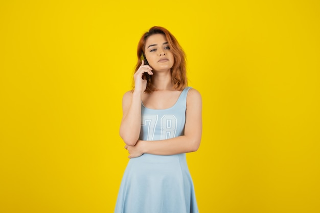 Chica joven pensativa hablando con teléfono en amarillo.