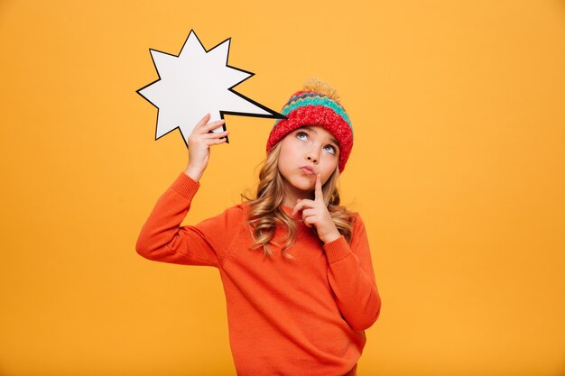 Chica joven pensativa en suéter y sombrero con estrella de discurso en blanco y mirando hacia arriba sobre naranja