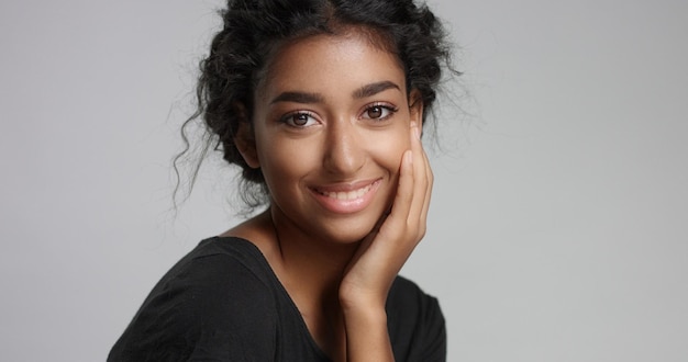 Chica joven con piel marrón clara perfecta y hermoso cabello negro rizado sonriendo a la cámara en el estudio