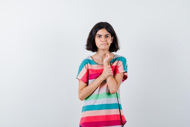 Chica joven poniendo la mano en el antebrazo en camiseta a rayas de colores y mirando seria. vista frontal.