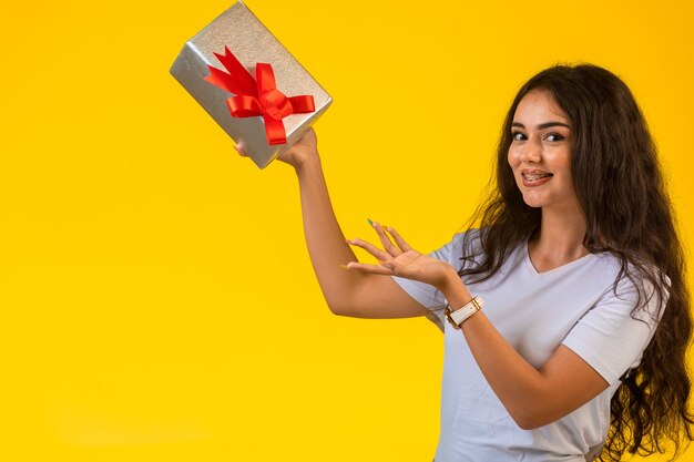 Chica joven posando con una caja de regalo en la mano y sonriendo.