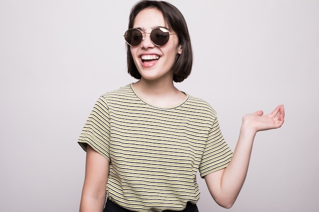 Chica joven posando en gafas de sol, estilo de moda aislado en gris. mujer hipster