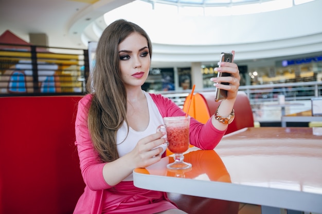 Chica joven posando con un teléfono y un refresco