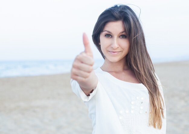 Chica joven con pulgar arriba en la playa