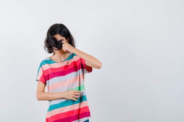 Chica joven que cubre la cara con el pelo en una camiseta a rayas de colores y se ve linda, vista frontal.